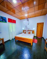 Un dormitorio con una cama de madera, un ventilador de techo, una lámpara en la pared, una puerta y una mesita.