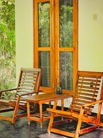 Una mecedora de madera y una silla de madera con una mesa frente a una ventana que da a zonas verdes.