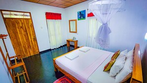 A bedroom with a bed, bedside table, chair, and a mosquito net. - Sunbird's Home  (Udawalawa)