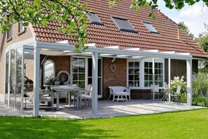 Ein Haus mit überdachter Terrasse, Ziegelaußenwand und Garten.