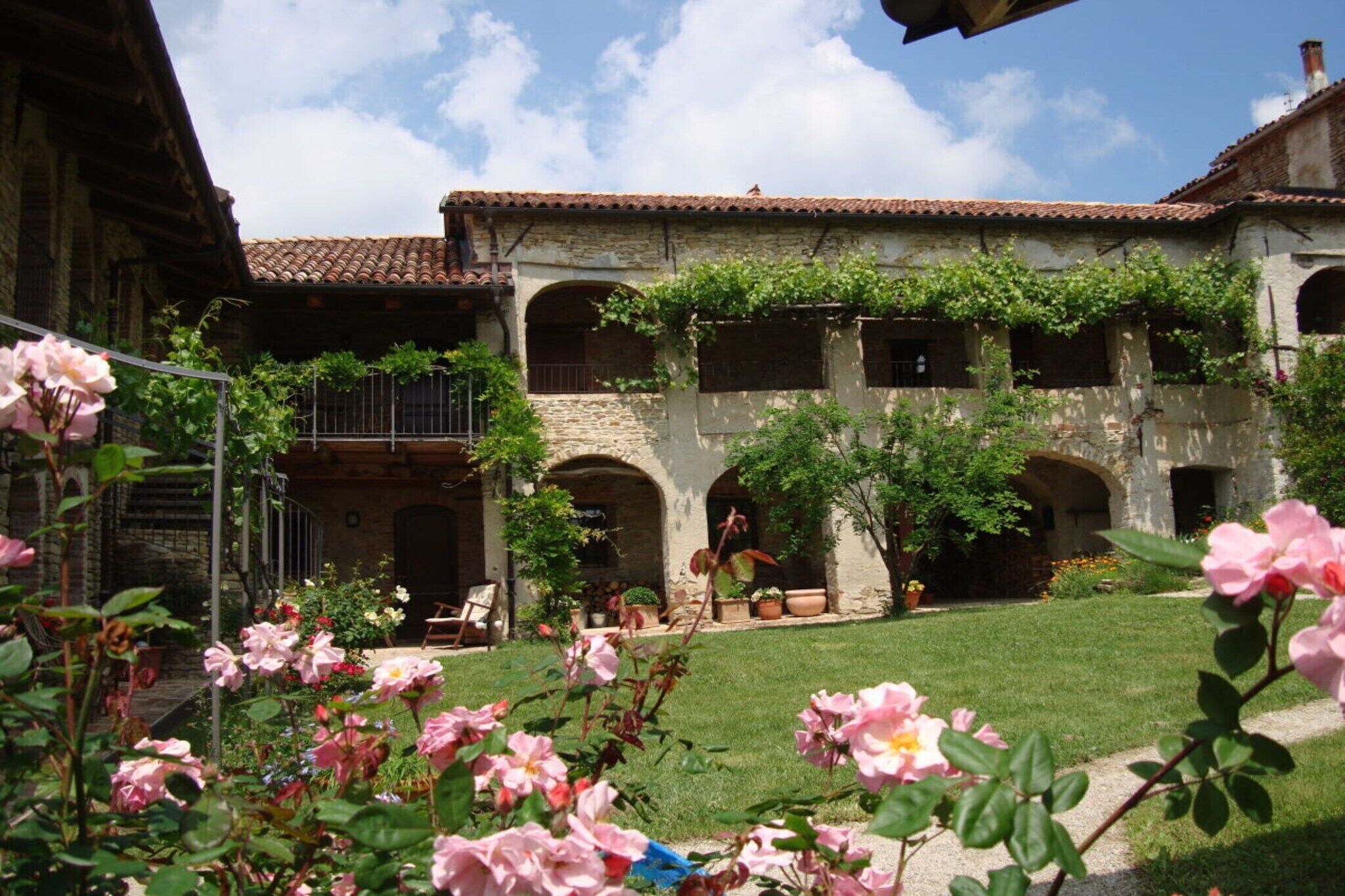 A courtyard with a building featuring arched windows and a tiled roof, surrounded by a well-maintained lawn and flowering plants.