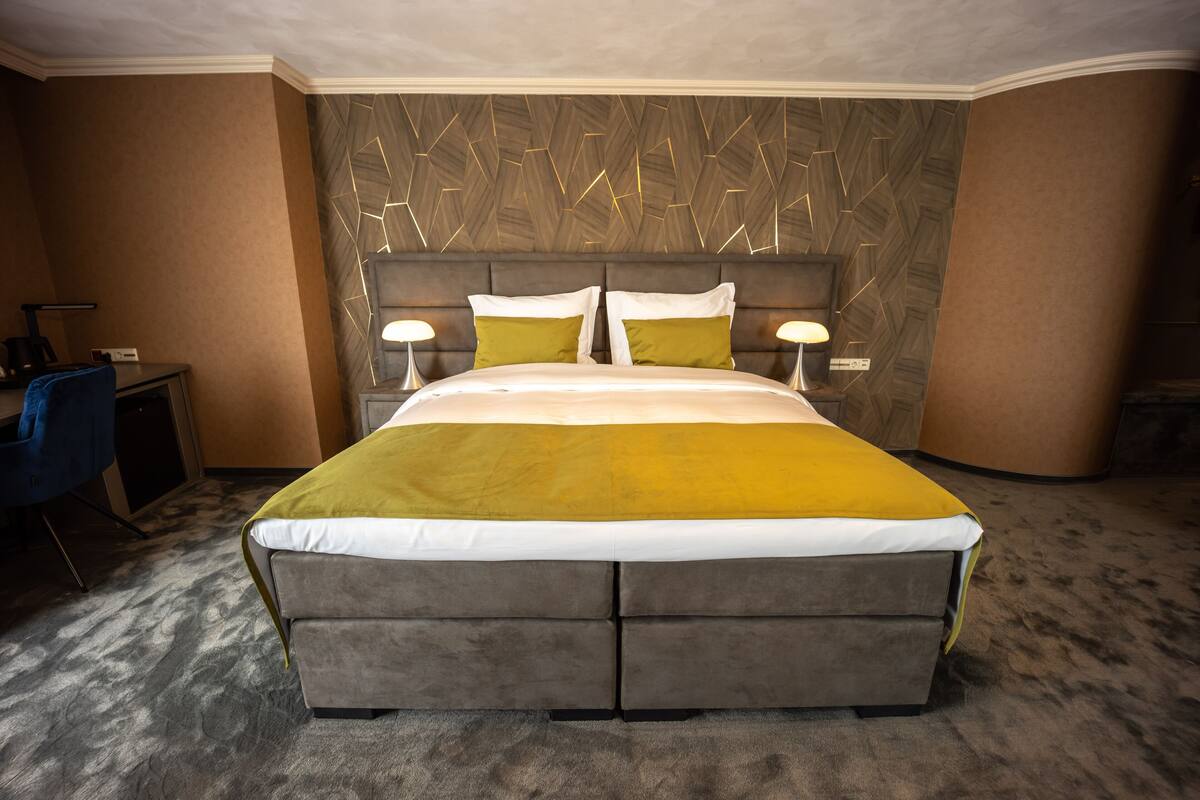 A modern hotel room with a large bed, two bedside tables with lamps, a desk, and a chair.