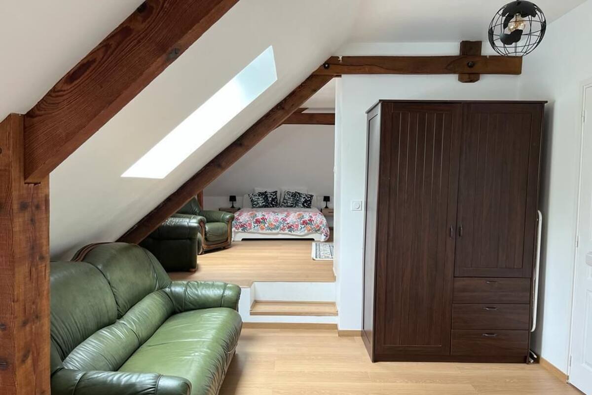 A loft bedroom with a sloped ceiling, a green leather sofa, a wooden wardrobe, and a bed with floral bedding.