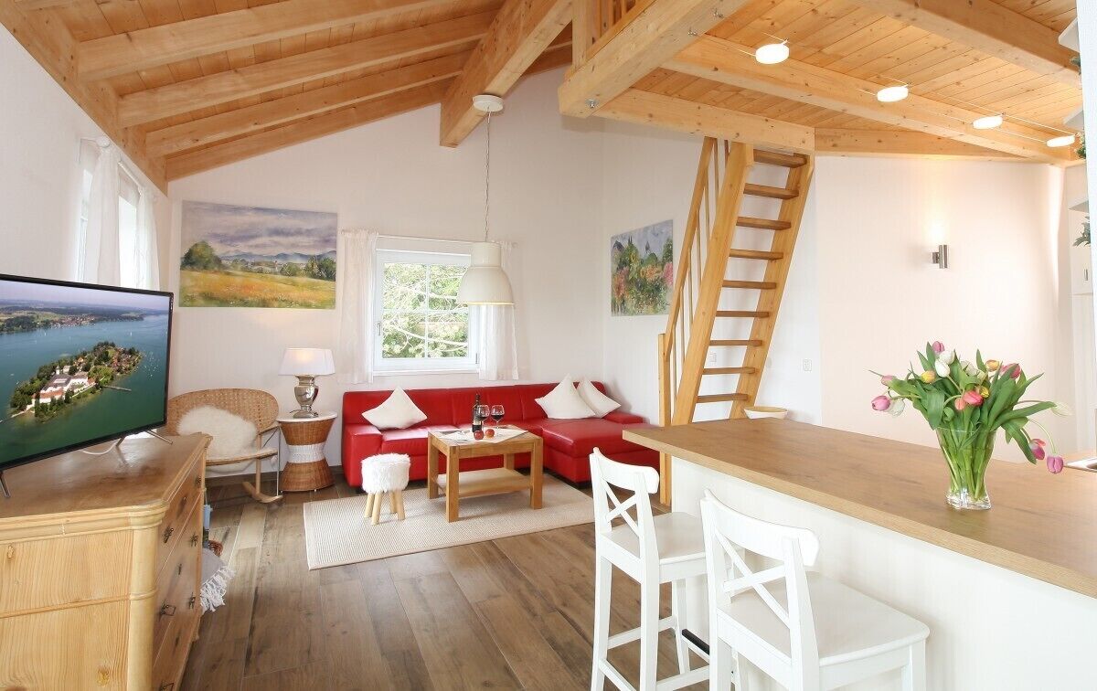 A cozy living room with a red sofa, wooden ceiling beams, a TV, and a wooden bar area.
