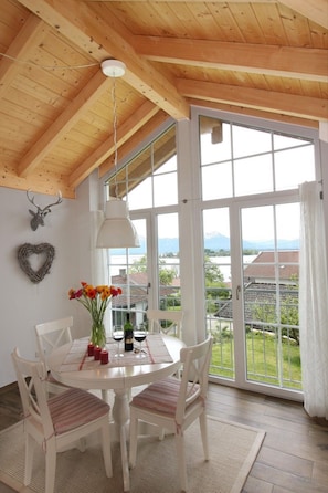 A dining area with a round table, white chairs, and a view of a mountainous landscape through large windows.
