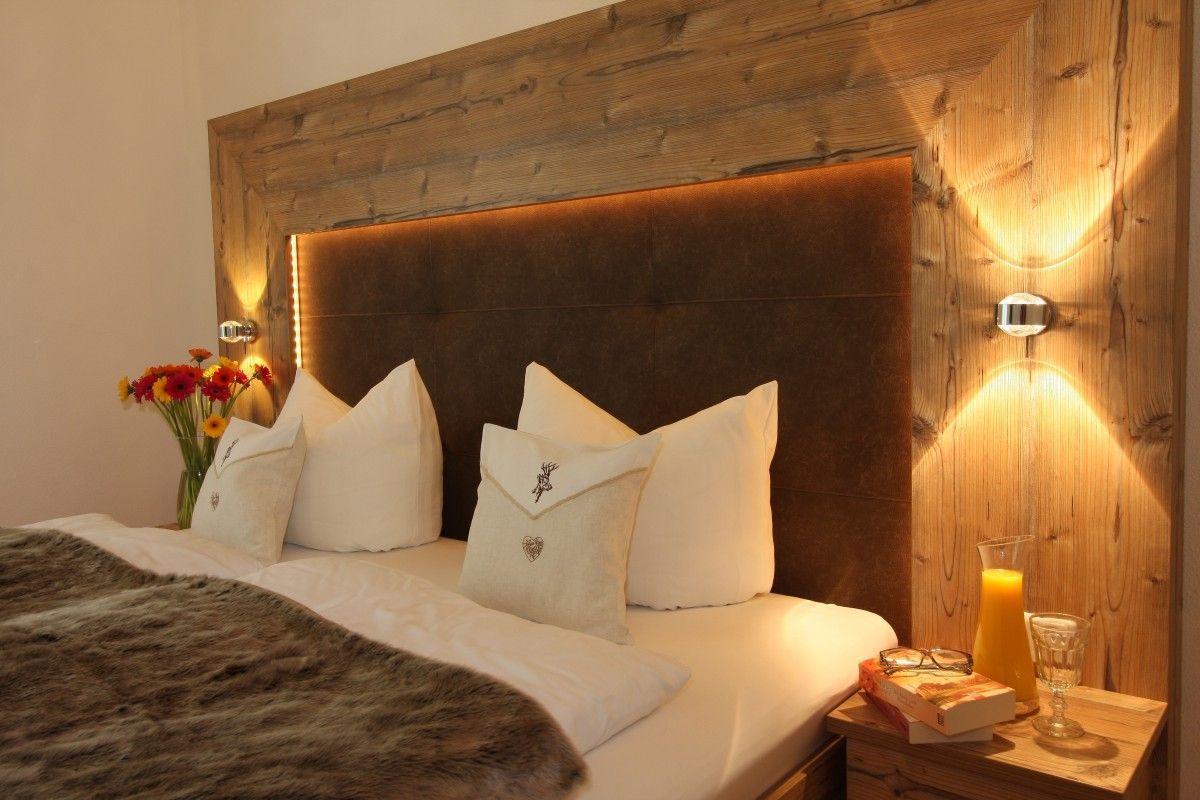 A bed with white bedding, a fur throw, and decorative pillows. A bedside table holds a book, a glass of orange juice, and a vase with flowers.