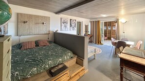 A cozy bedroom with a bed, a desk, and a chair. There is a wooden ceiling and a wall with artwork. - Plein la vue (Saint-Pierre)