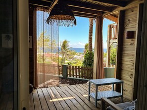 A wooden deck with a table and bench, overlooking a coastal area with palm trees and houses.