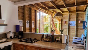 A kitchen with wooden cabinets, a gas stove, a coffee maker, and a window with curtains. - Plein la vue (Saint-Pierre)