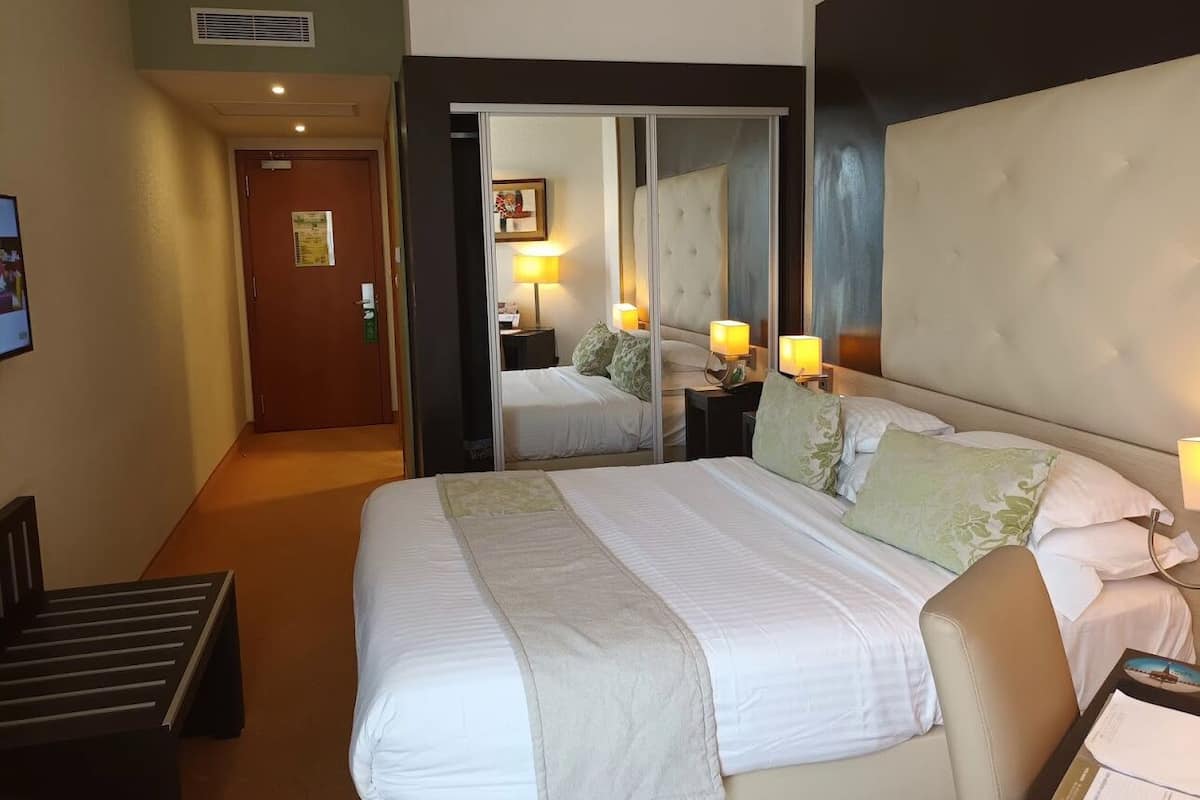 A hotel room with a large bed, a mirror, a desk, and a chair.