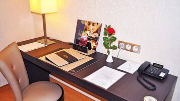 Un mostrador de recepción de hotel con una lámpara de escritorio, un teléfono, un florero con una rosa, un cuadro enmarcado y un bloc de notas.