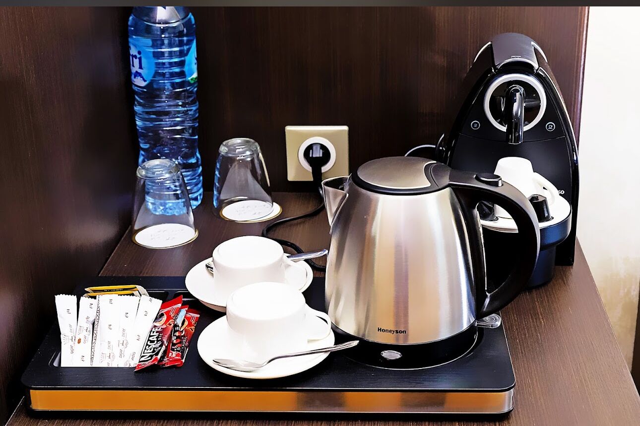 A hotel room with a coffee station including a kettle, cups, and a tray with snacks and a water bottle.