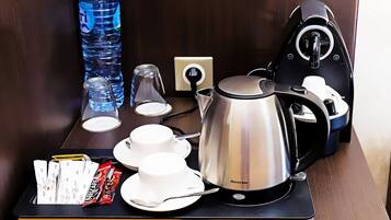 Habitación de hotel con estación de café que incluye un hervidor, tazas y una bandeja con aperitivos y una botella de agua.
