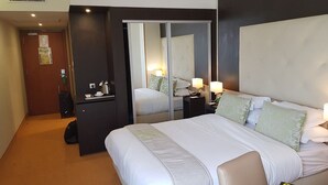 Una habitación de hotel con una cama grande, lámparas de noche, un escritorio con una silla y un espejo.