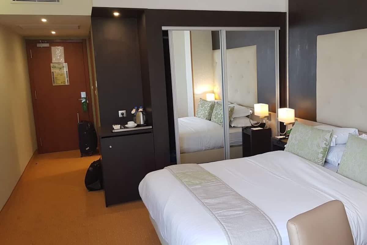 A hotel room with a large bed, bedside lamps, a desk with a chair, and a mirror.
