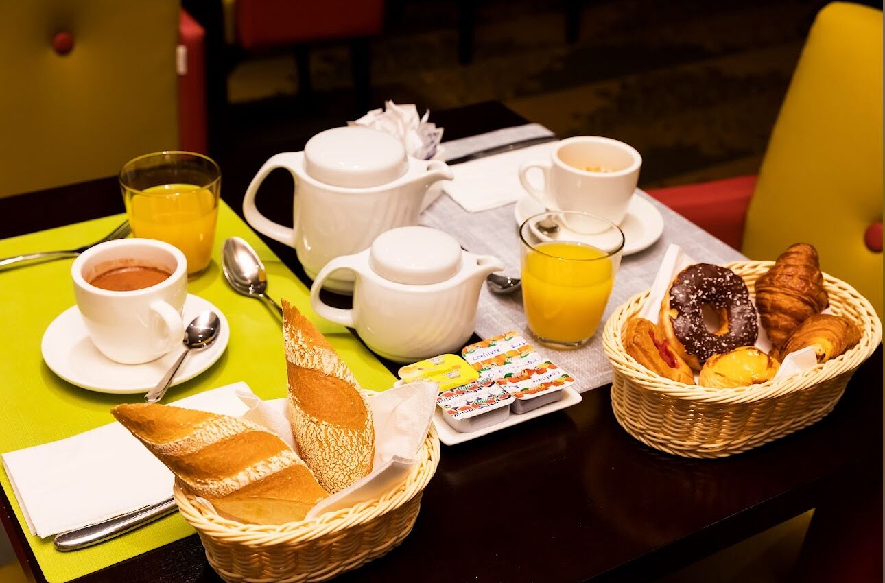 A breakfast setup with bread, pastries, coffee, and juice on a table.