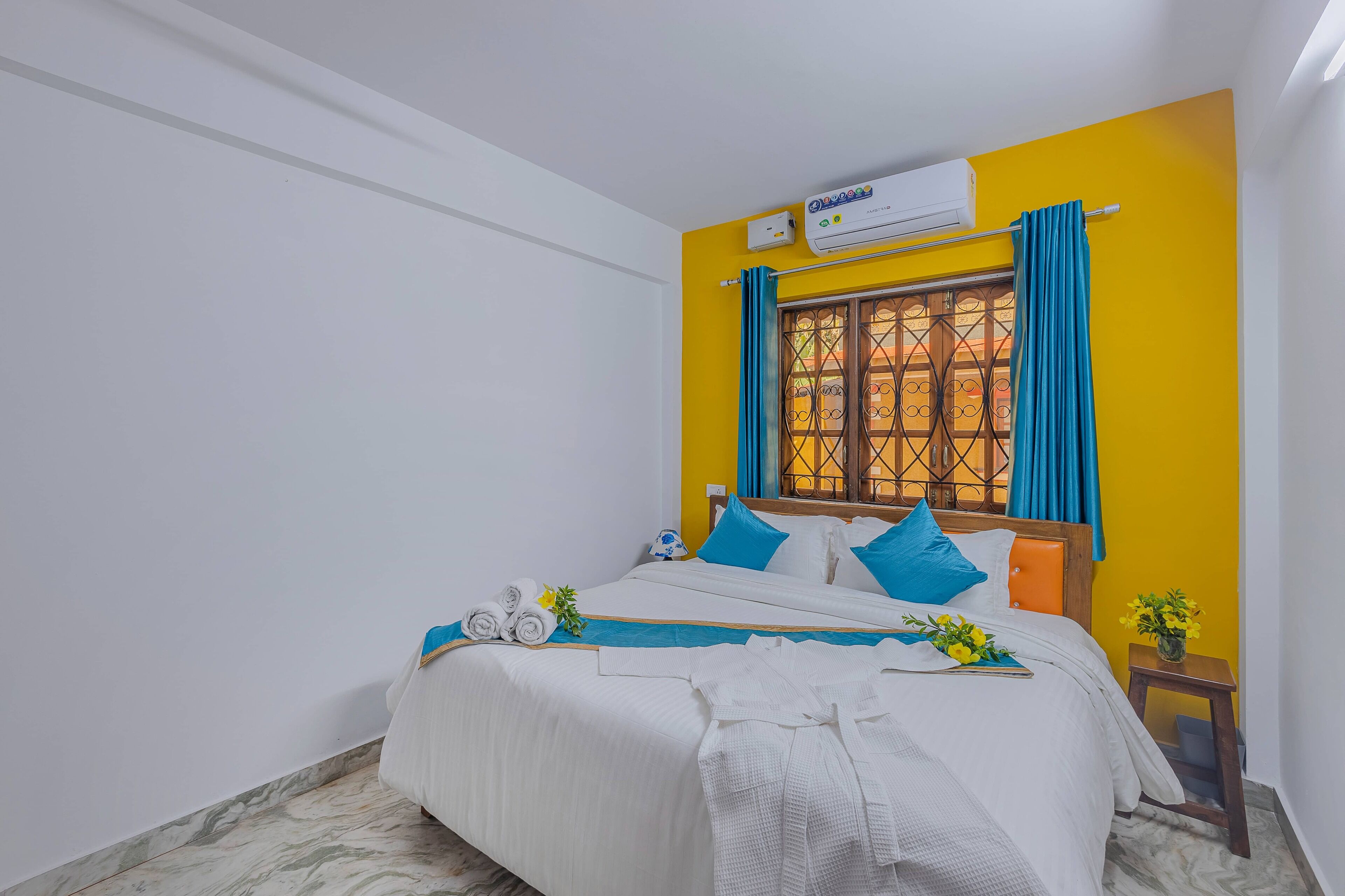 Una cama bien tendida con ropa de cama azul y blanca, una ventana con cortinas azules y un equipo de aire acondicionado en la pared.