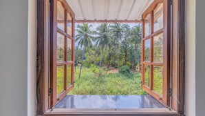 A view through an open window with wooden frames, revealing a lush outdoor area with palm trees and greenery. - The Sequeira Guest House (Majorda)
