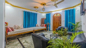 A room with a sofa bed, a black leather couch, a ceiling fan, and a wooden door. - The Sequeira Guest House (Majorda)