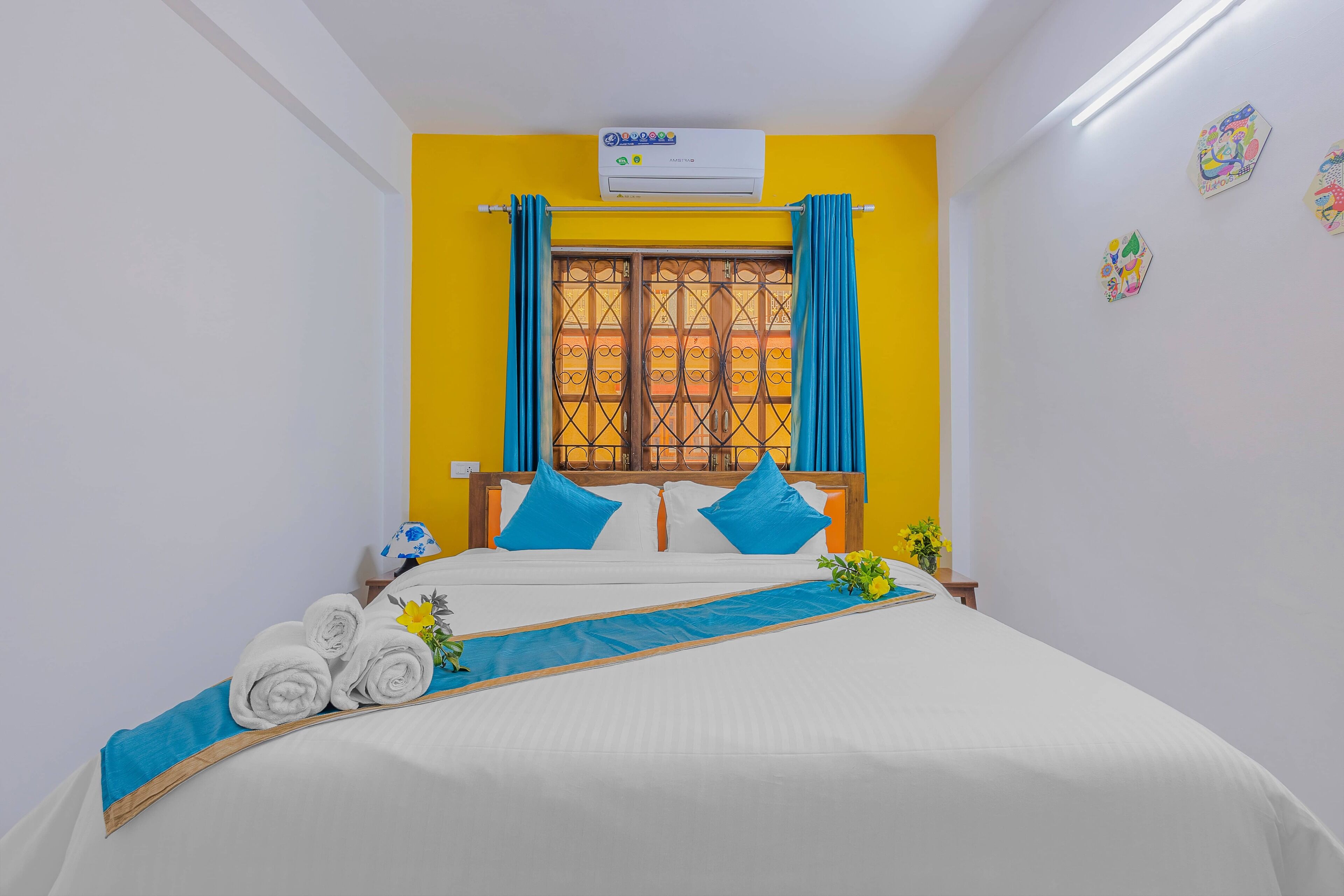 A hotel room with a bed, a window with curtains, an air conditioner, and a wall with artwork.