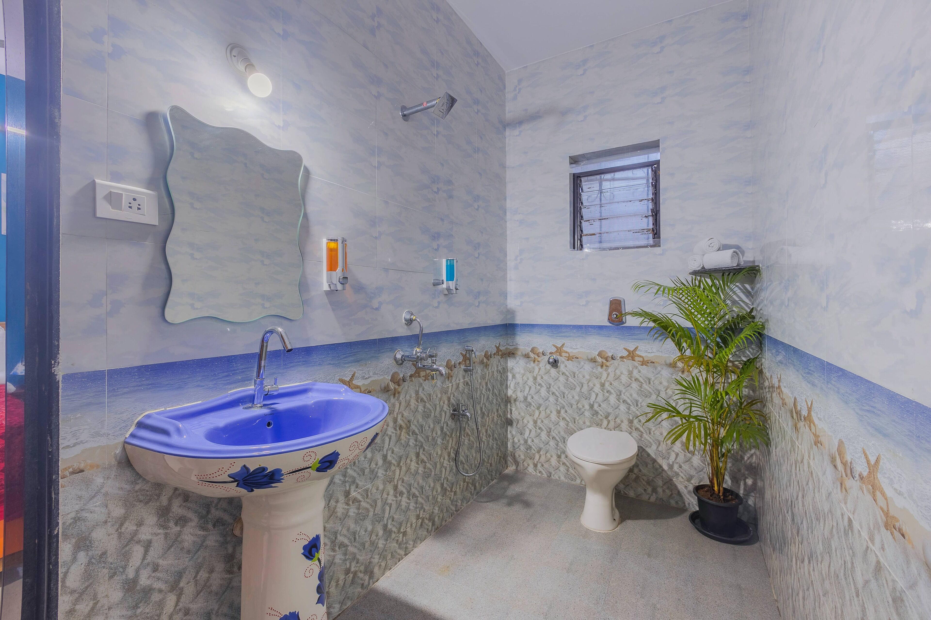 Un baño con lavamanos azul, inodoro, ducha y una ventana pequeña.