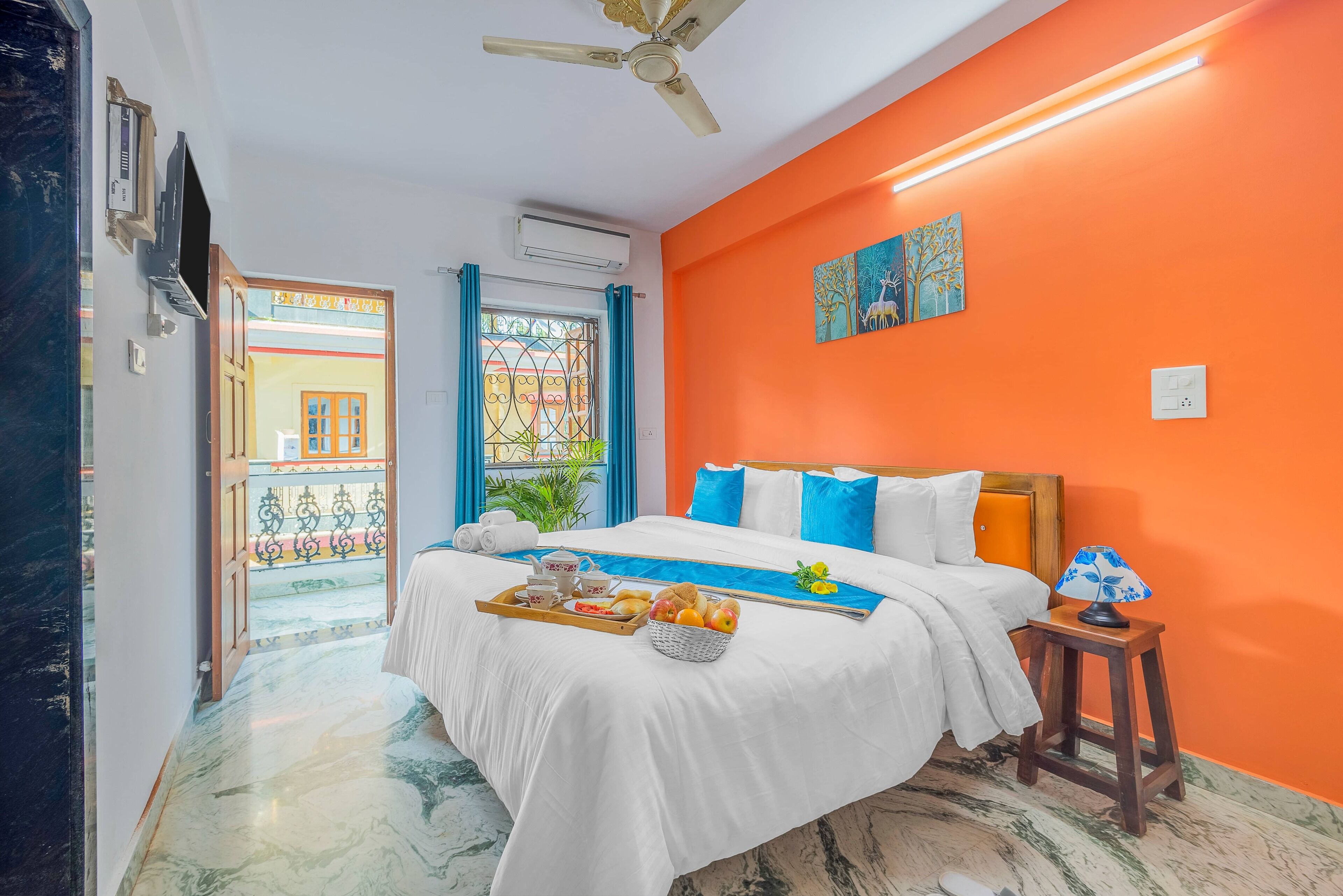 A hotel room with a bed, a tray of fruits, a lamp, and a ceiling fan.