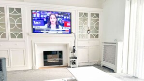 A living room with a flat-screen TV mounted above a fireplace, white cabinetry, and a white coffee table. - Zen 8-Bedroom Den in Edgbaston (Birmingham)