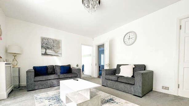 A modern living room with two grey sofas, a white coffee table, and a blue and white rug. - Zen 8-Bedroom Den in Edgbaston (Birmingham)