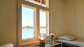 Een kamer met een bed, een nachtkastje met een lamp en een raam met uitzicht op water.