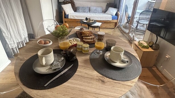 Un coin repas avec une table ronde mise pour le petit-déjeuner, un canapé surmonté d’un tableau représentant un cerf, et un téléviseur sur le côté droit.