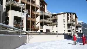 Un immeuble à plusieurs étages doté de balcons, d’un toit enneigé et surplombant un ciel dégagé.