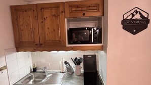 Une cuisine compacte avec des meubles en bois, un four à micro-ondes, un évier et un petit réfrigérateur.