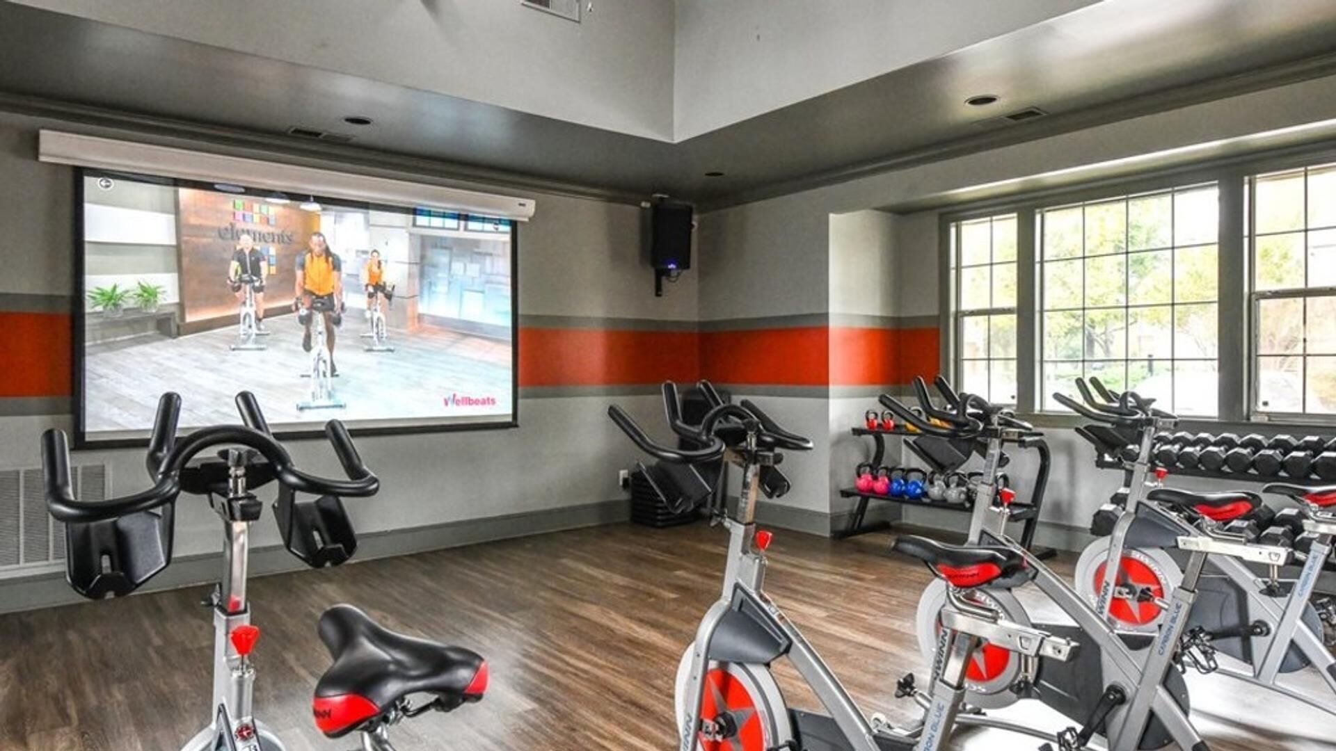Un gimnasio con bicicletas estáticas, una pantalla de proyección y mancuernas.