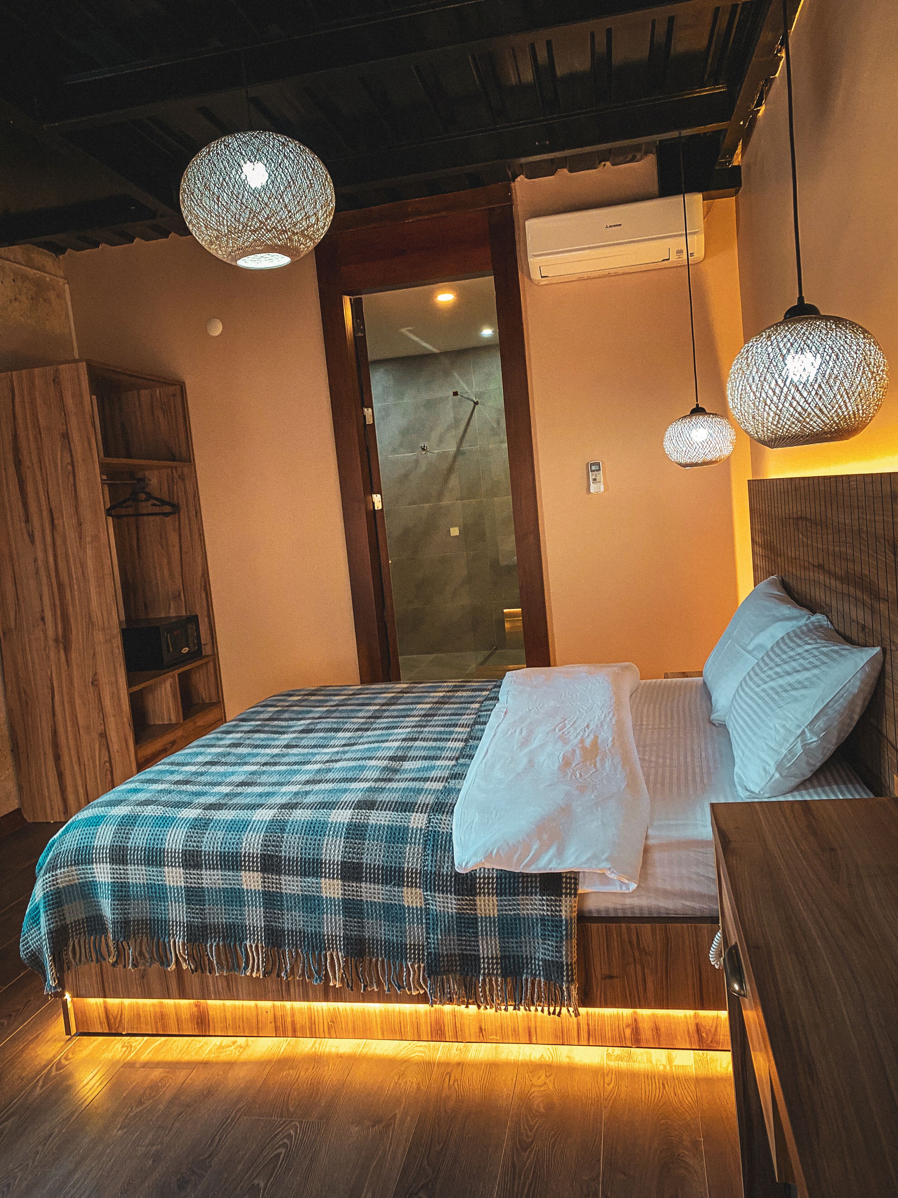 A bedroom with a wooden bed, a wooden wardrobe, and two hanging light fixtures.