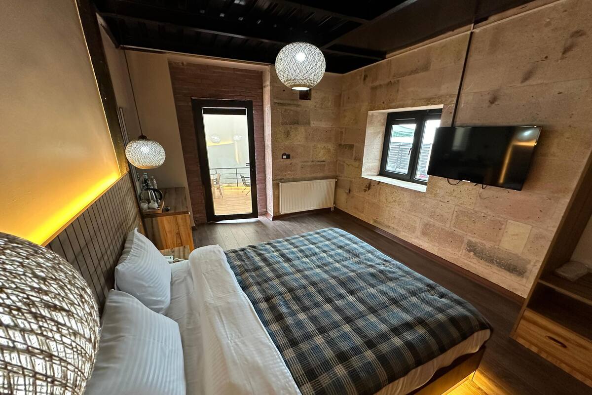 A modern bedroom with a large bed, a television mounted on the wall, and a view of the outdoors through a sliding door.