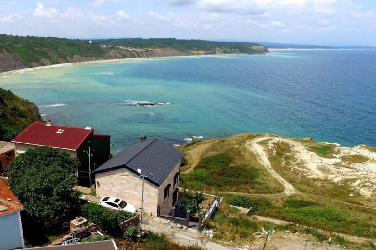 A coastal property with a view of the sea, a house with a red roof, and a white car parked in front.