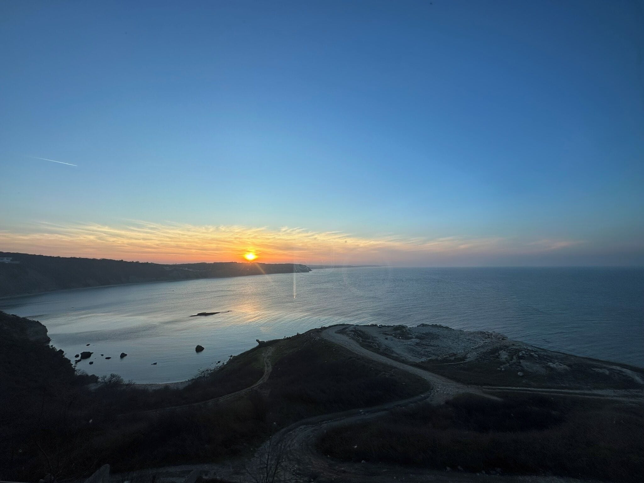 A coastal sunset view with a winding road leading to the sea.