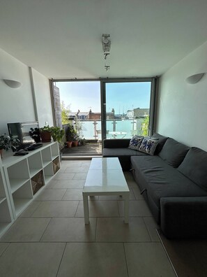 A modern living room with a sofa, a coffee table, a TV, and a balcony with a view of the city. - Bright And Airy Islington Apartment (London)