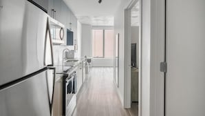 Une cuisine moderne dotée d’appareils électroménagers en acier inoxydable, un coin repas avec une table et des chaises, et une grande fenêtre laissant entrer la lumière naturelle.