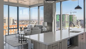 Eine moderne Küche mit einer großen Kochinsel, einem Essbereich mit Sofa und Tisch sowie großen Fenstern mit Blick auf die Stadt.