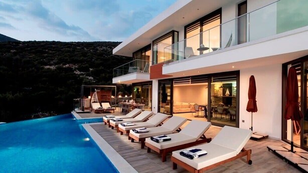 Un hotel moderno con un área de descanso junto a la piscina, asientos al aire libre y vistas del paisaje circundante.