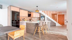 Una cocina moderna con una isla central, suelo de madera y una escalera que sube a otro nivel.