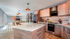 Una cocina moderna con una isla central, electrodomésticos integrados e iluminación colgante.