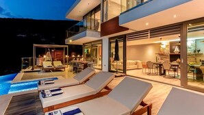 Un hotel moderno con zona de piscina, mobiliario exterior y un interior bien iluminado.