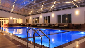 An indoor swimming pool with clear blue water, surrounded by lounge chairs and a high ceiling with exposed beams. - Windermere Hotel (Shillong)