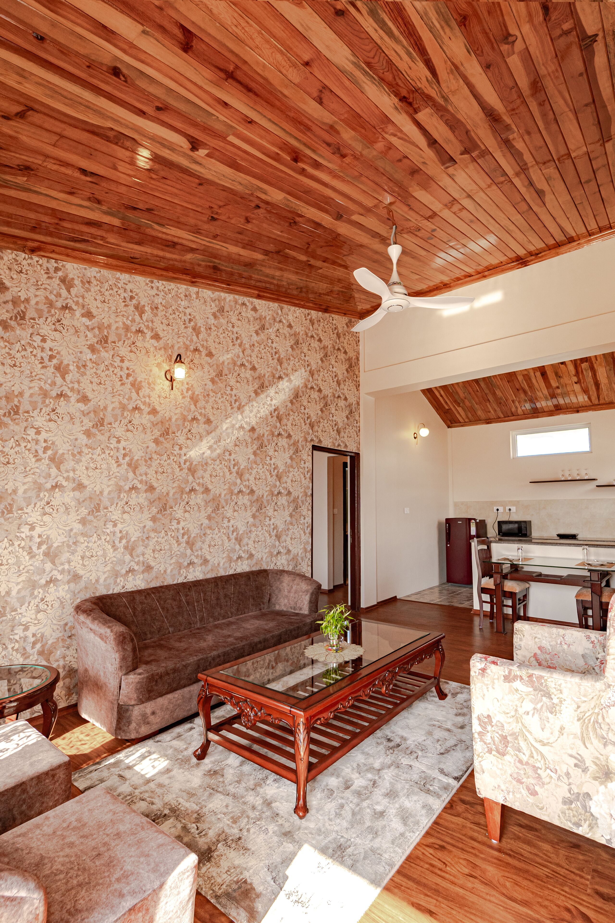 A spacious living area with a wooden ceiling, a sofa, a coffee table, and a dining table with chairs.