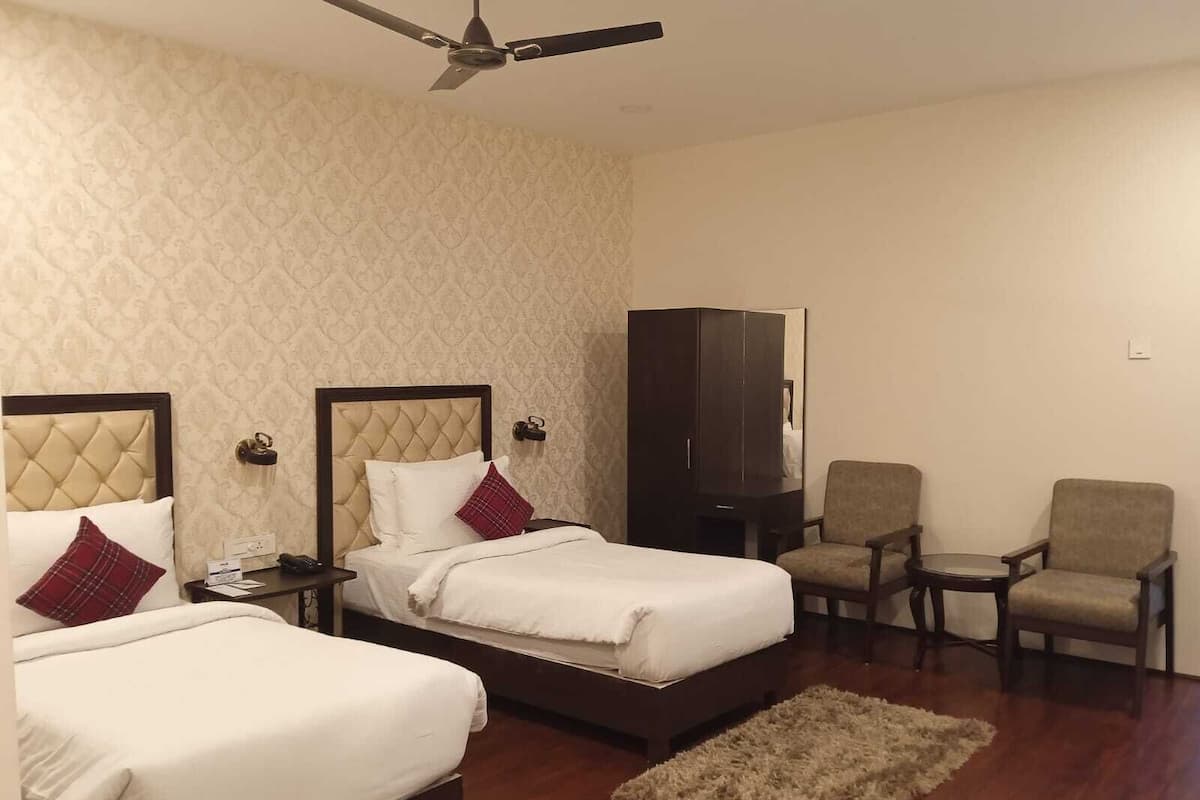 A hotel room with two beds, a ceiling fan, a wardrobe, and a seating area with chairs.