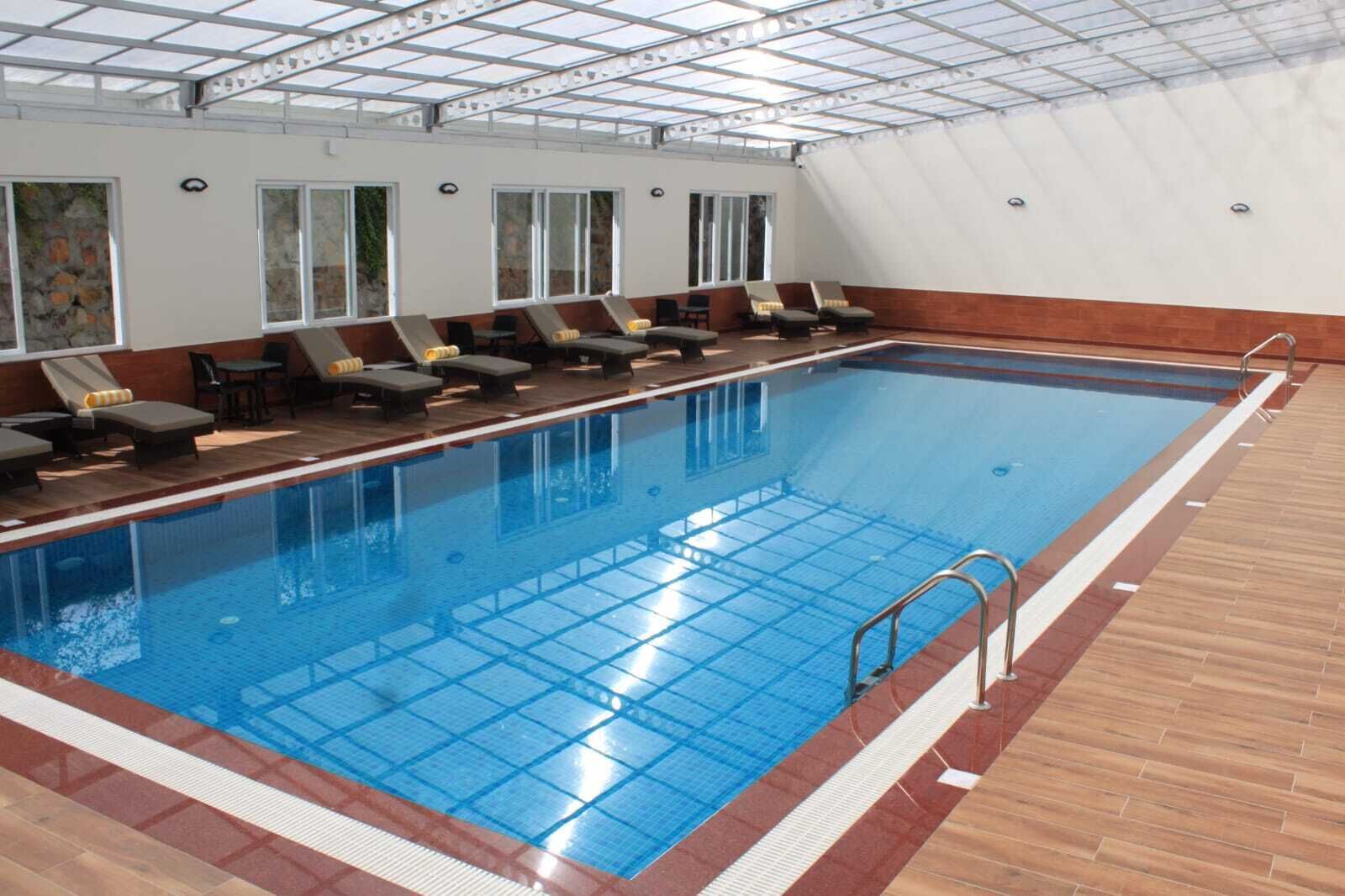 Una piscina interior con suelo de baldosas, una escalera de piscina y sillones de descanso a un lado.