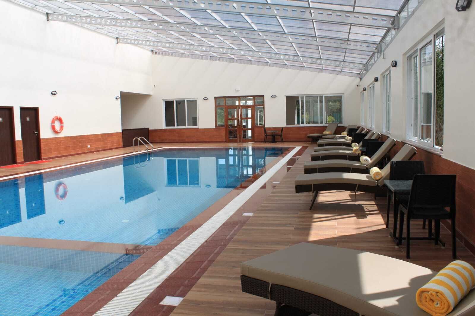Una piscina interior con sillones de descanso y techo de cristal.