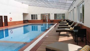 Una piscina interior con sillones de descanso y techo de cristal.